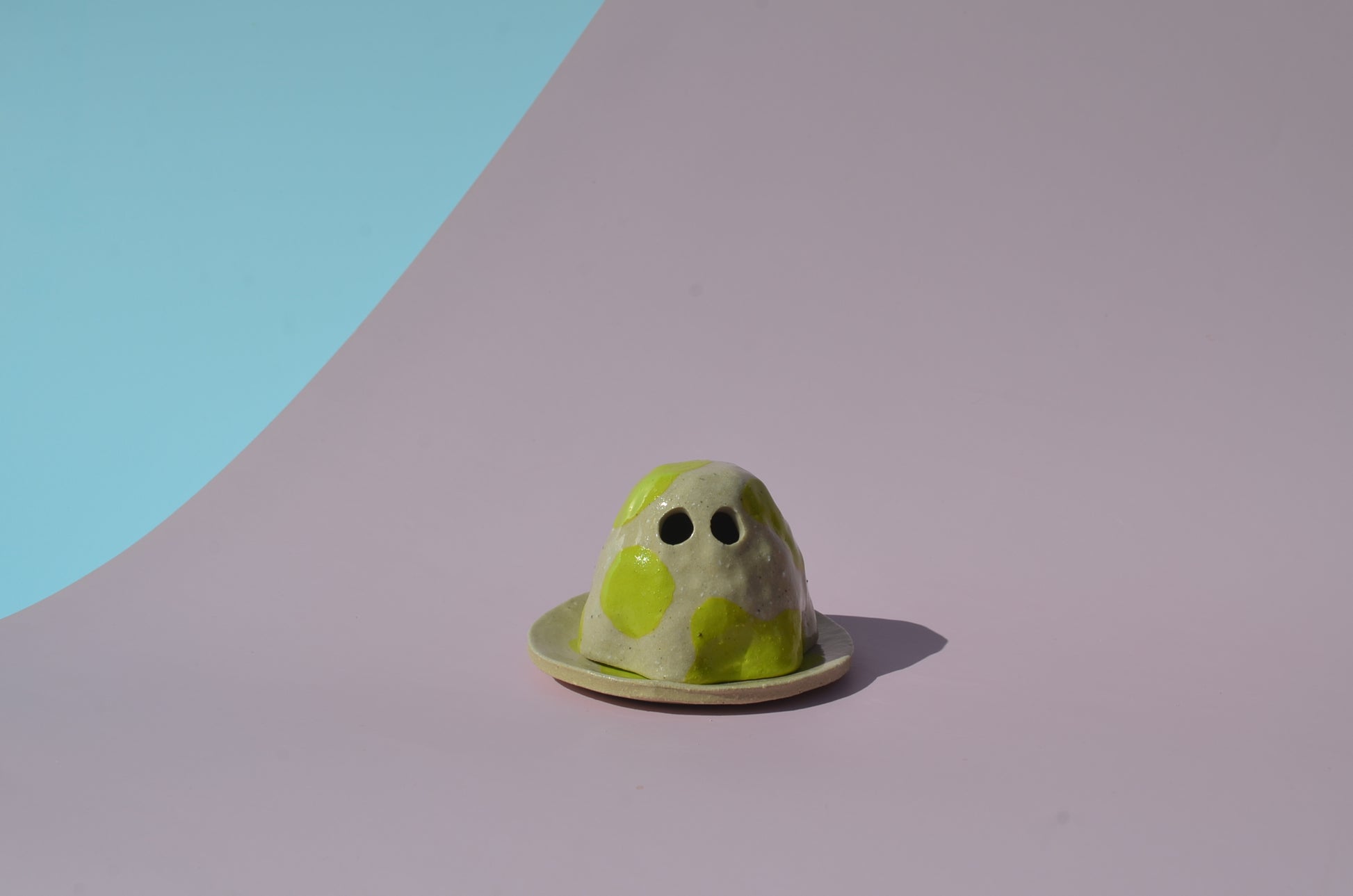 Picture of a handmade ghost figurine with its eyes carved out, sitting on a small round tray and painted in a lime green cow spot design.