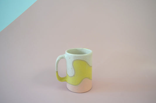 Picture of a handmade mug with a wavy cut out design of three segments, one painted white, one yellow and the third one pink.