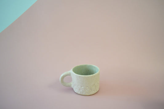 Picture of a small handmade espresso mug that has a dappled carved pattern along the bottom, and is painted white on the exterior and light blue on the inside.