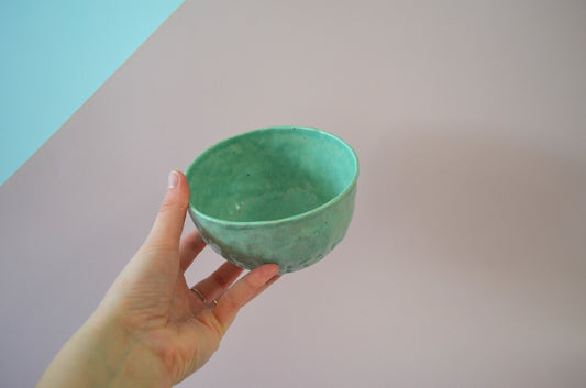 Picture of a handmade small snack bowl being held up to show it's size, painted in a light green.